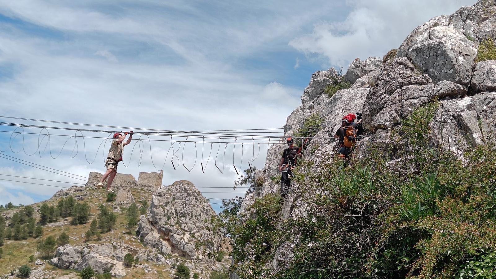 A person (Alan Carr) shuffles precariously along a himalayan wire bridge