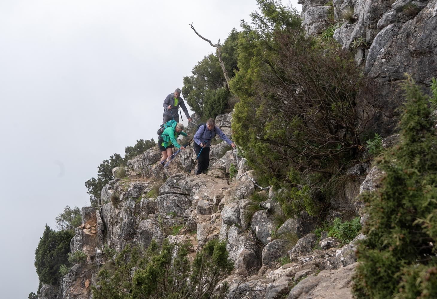 3 people descend some airy slabs holding onto a chain for safety