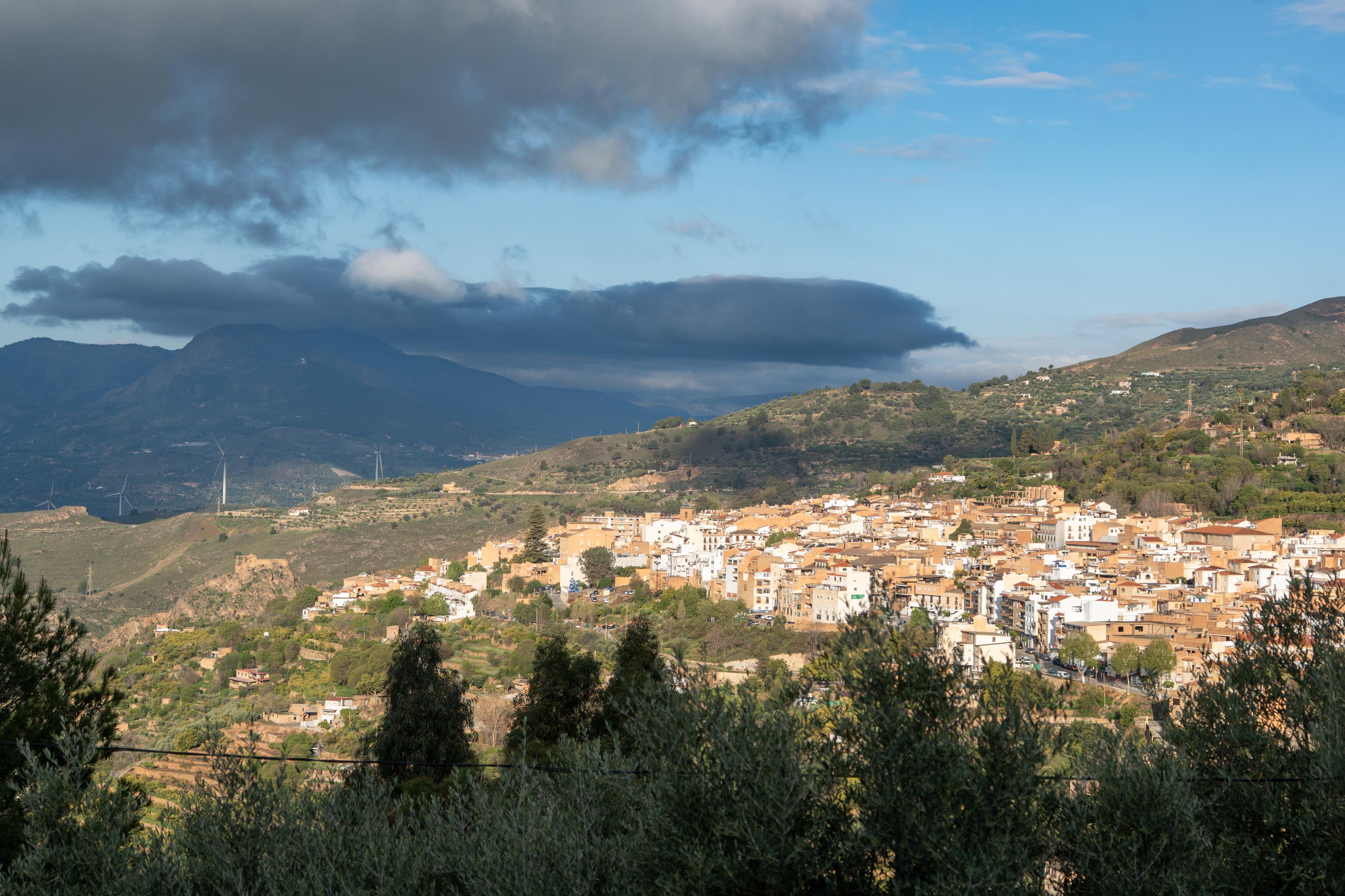 A Spanish town is highlighted in the morning sun. Behind are threatening rain clouds approaching