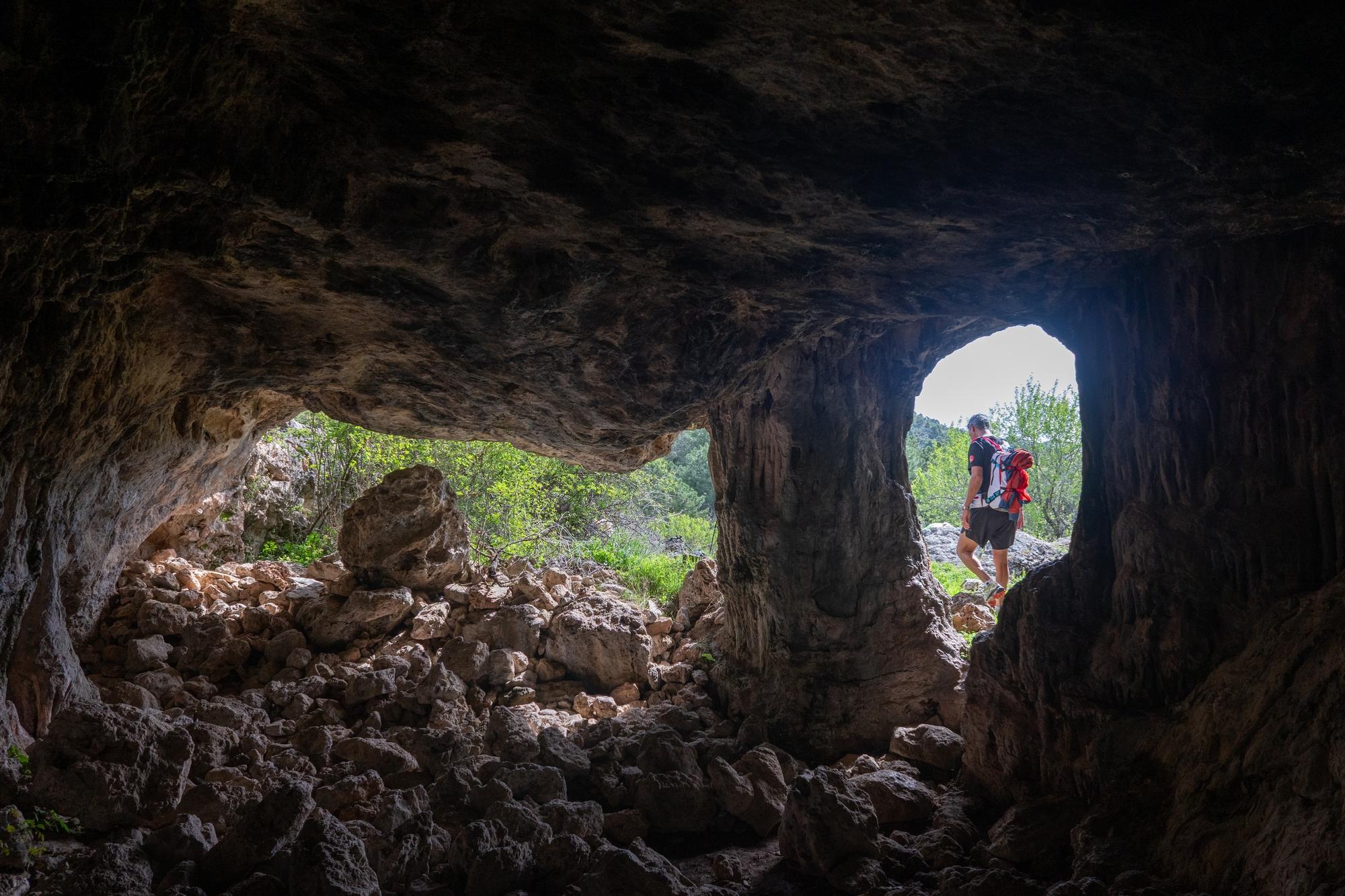 Inside a dark cave with 2 openings. The right opening has a person passing by