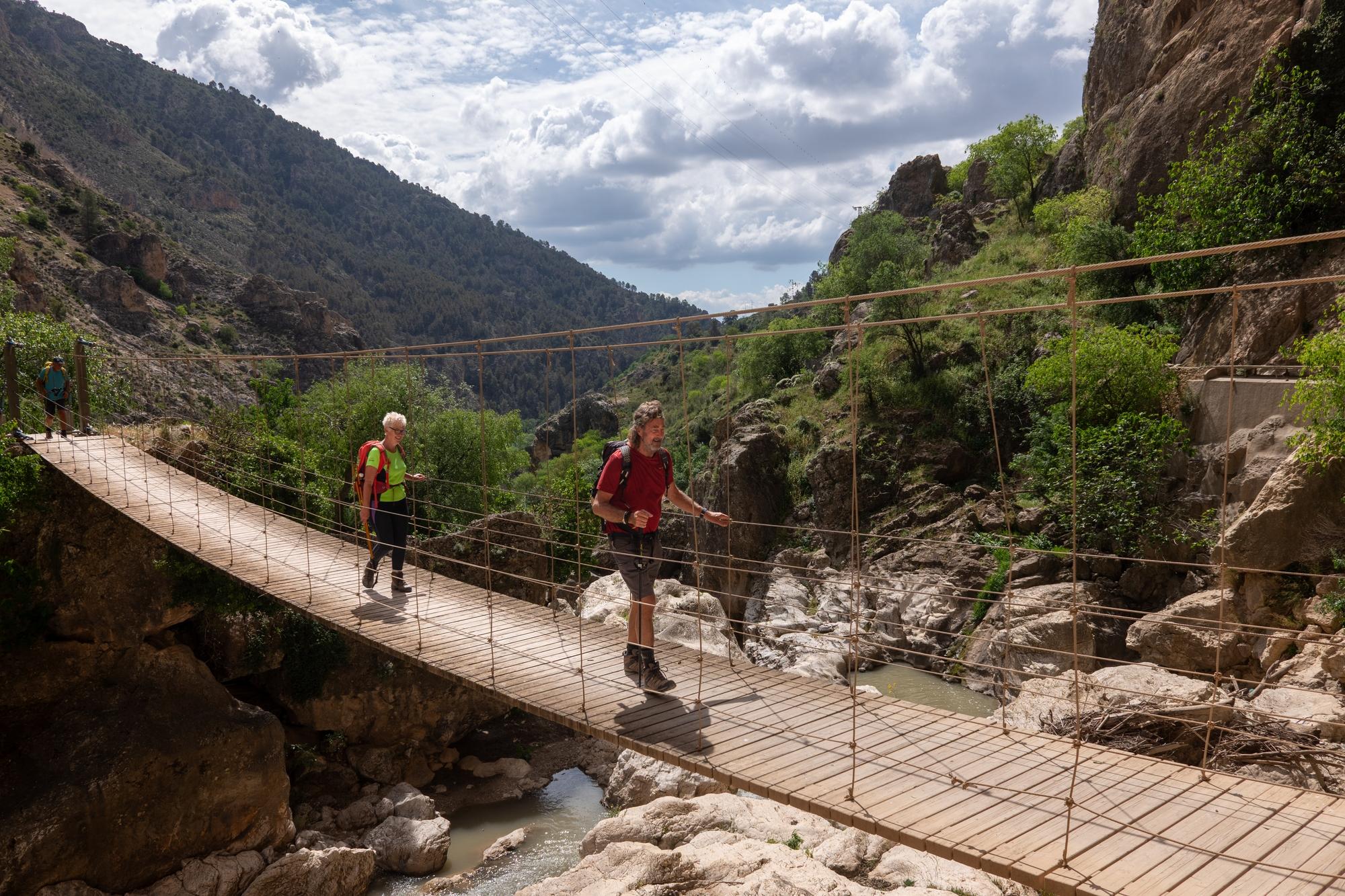 Two hikers cross a wood/wire bridge high above a river