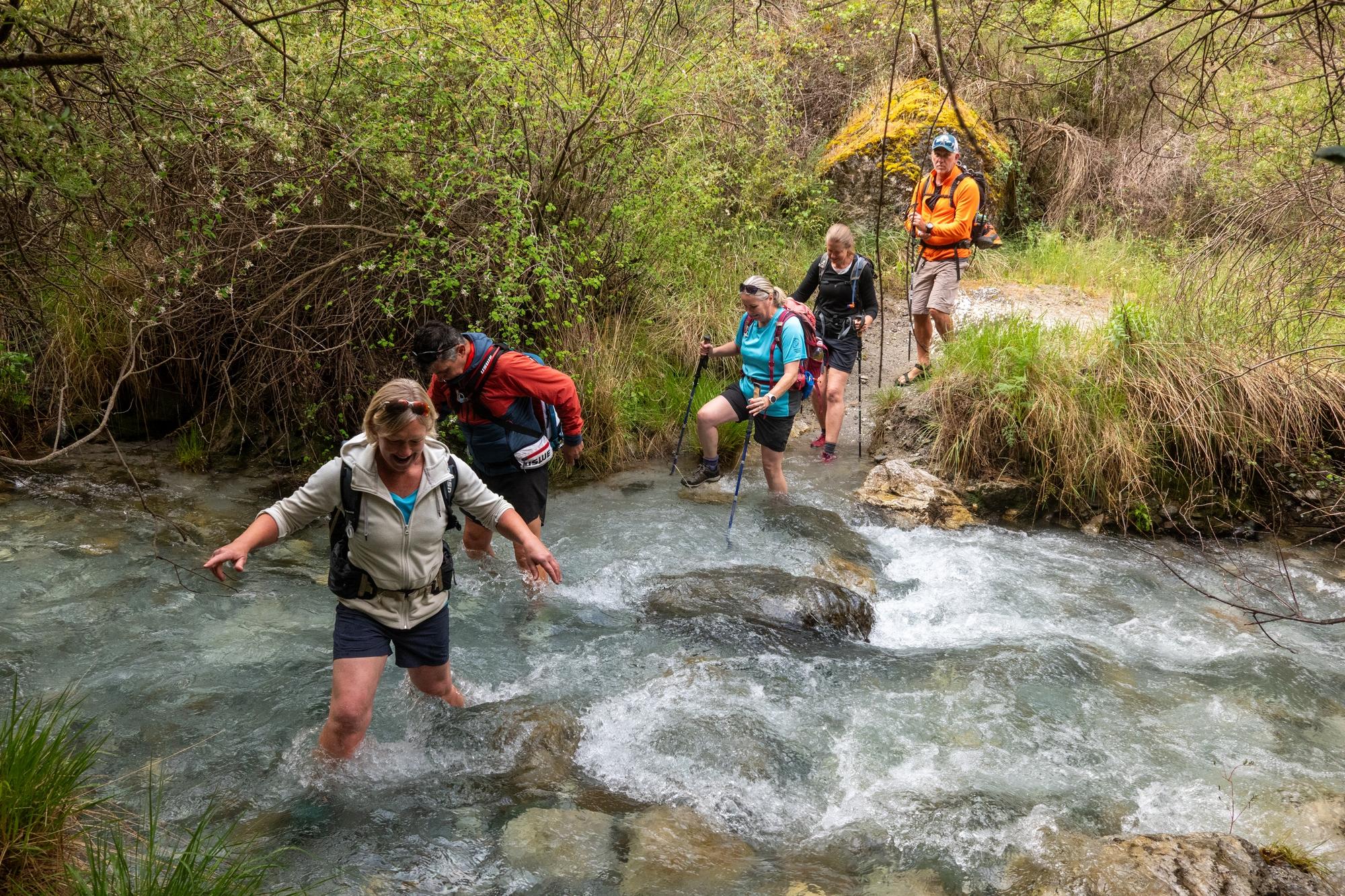 A line of hikers attempting to cross a fast flowing stream