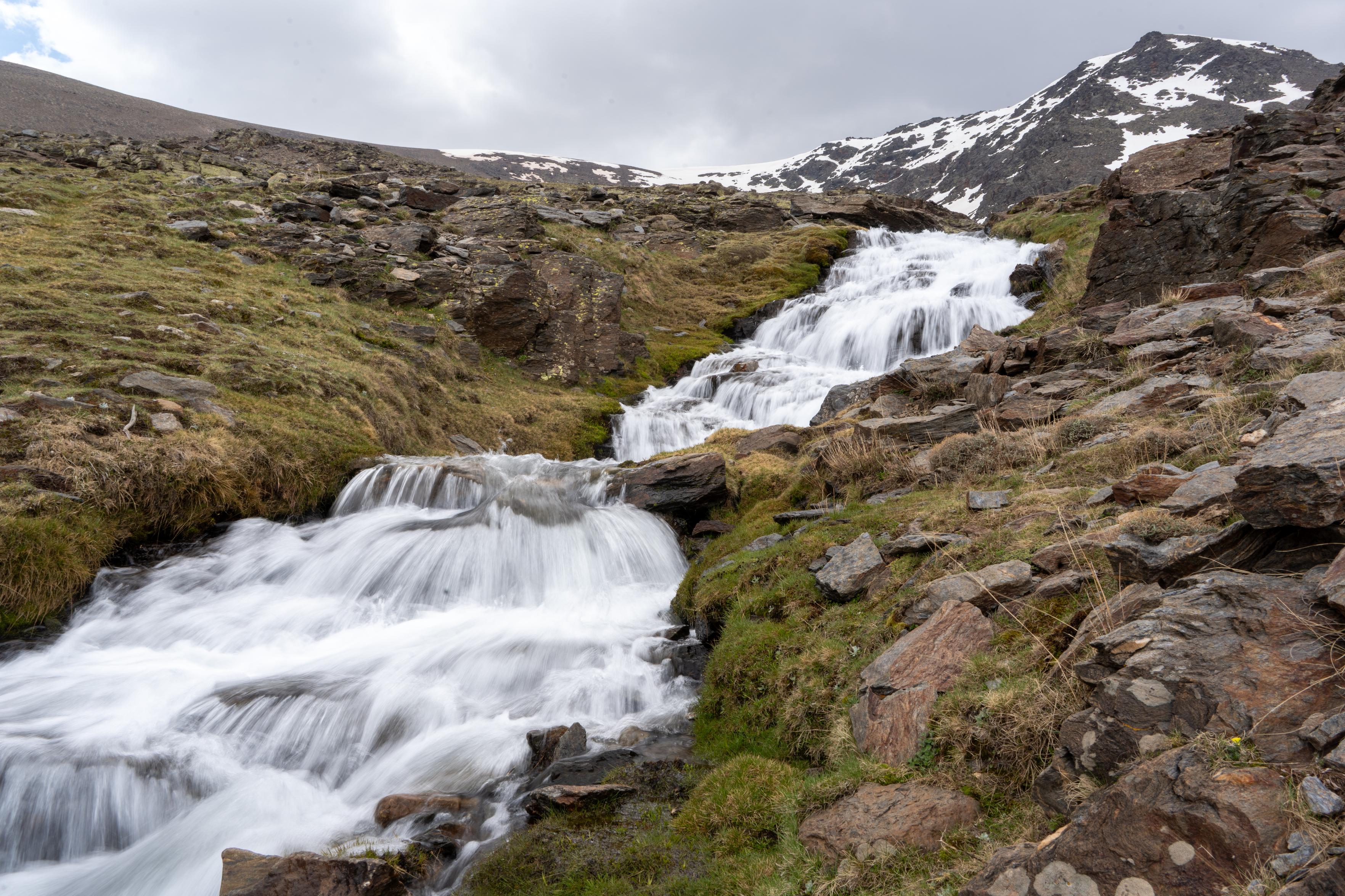 A series of two waterfalls dropping down out of the lip of a valley. Behind is a mountain with snow
