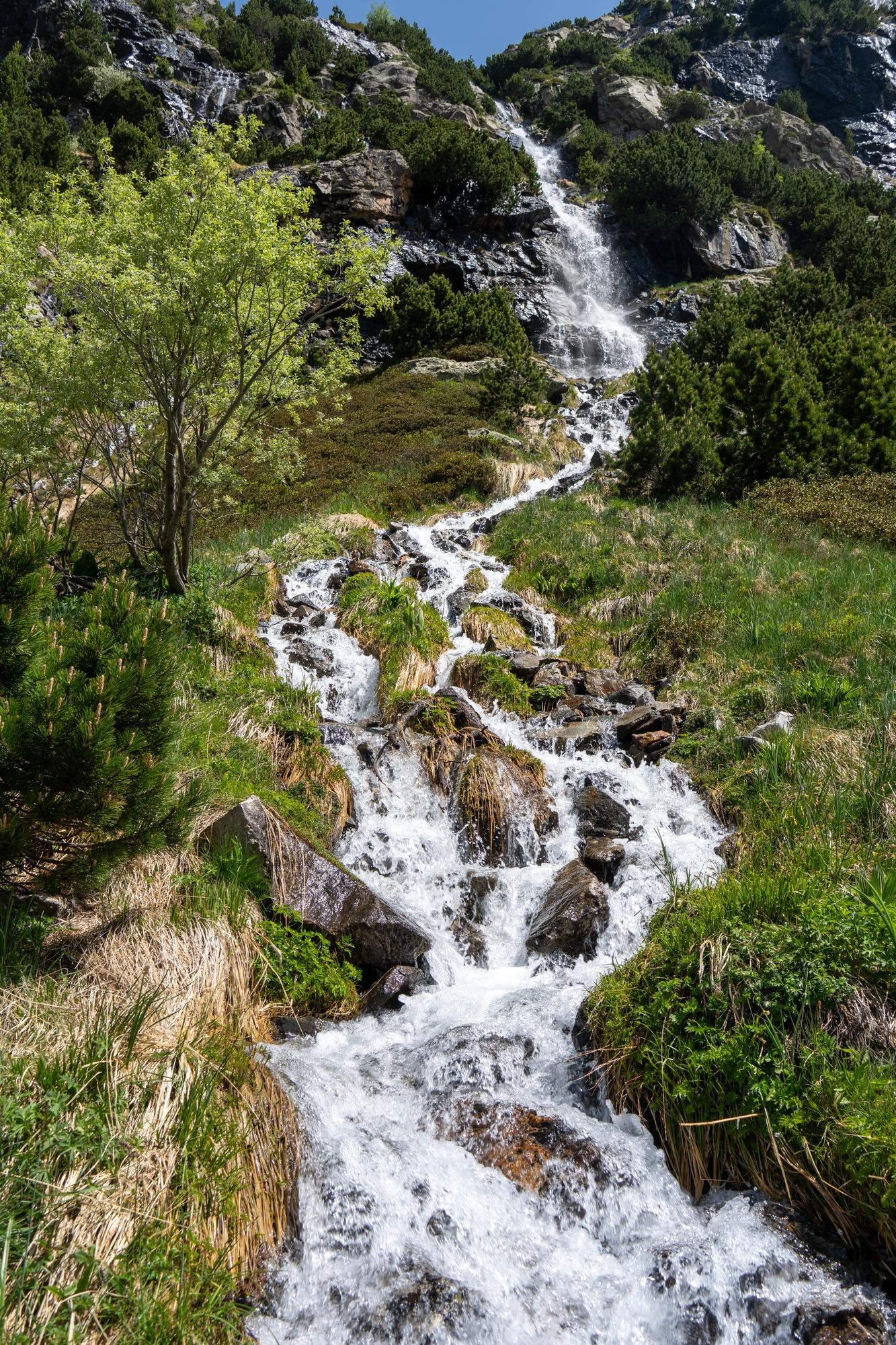 A river drops over a series of spectacular waterfalls, the highest one being at the top. The banks are rich in green vegetation