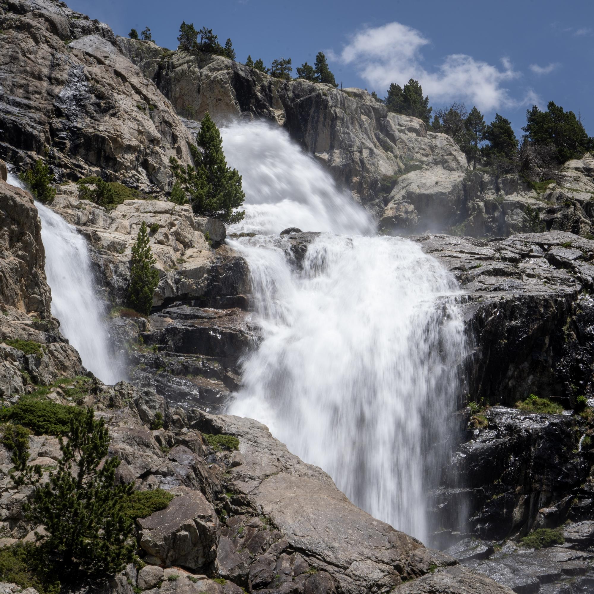 A river drops over a series of spectacular waterfalls between vertical rock walls. and continues downstream over rocks and boulders