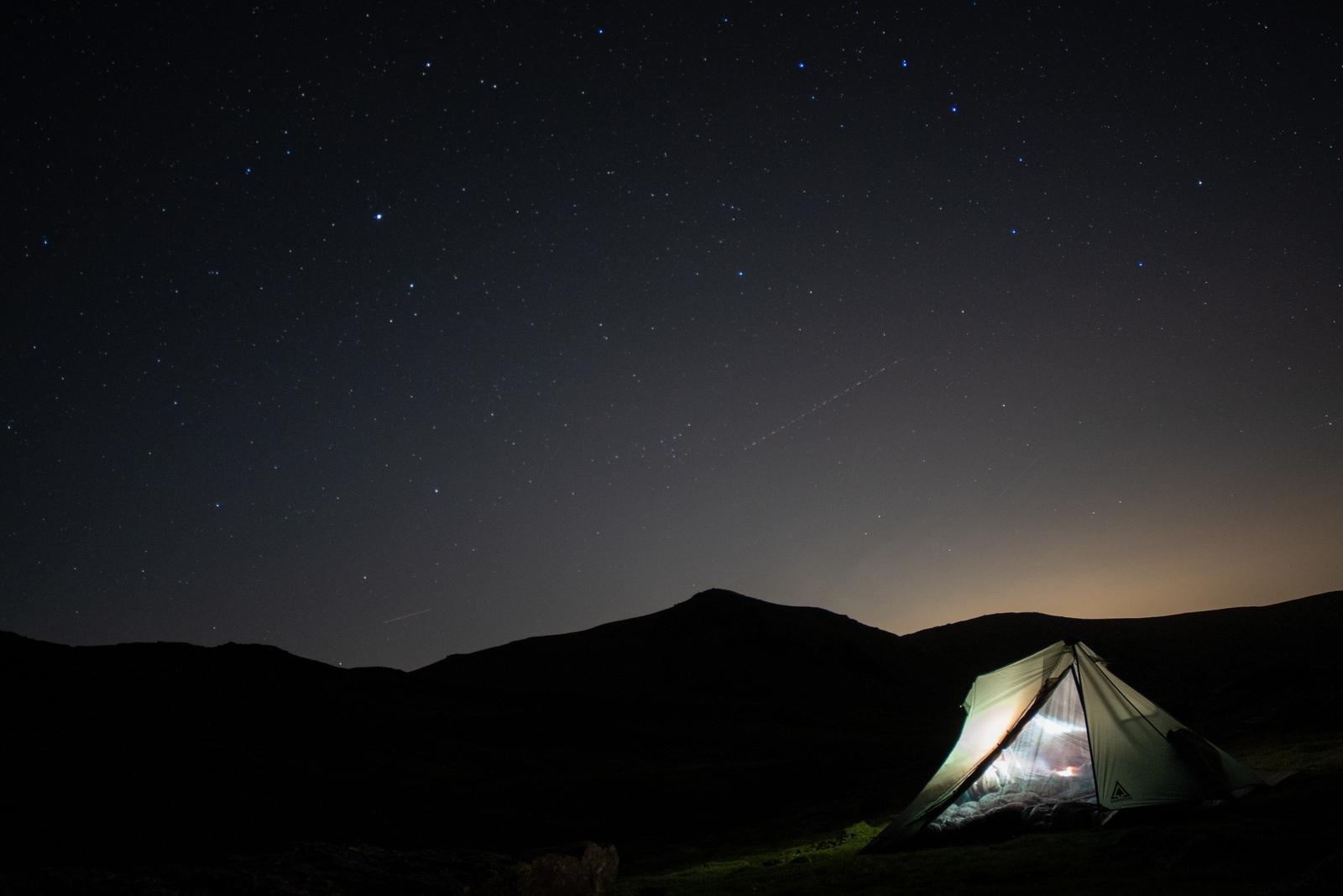 The last light of the sunset is fading and the stars appear over to the west. A tent is illuminated by headtorch
