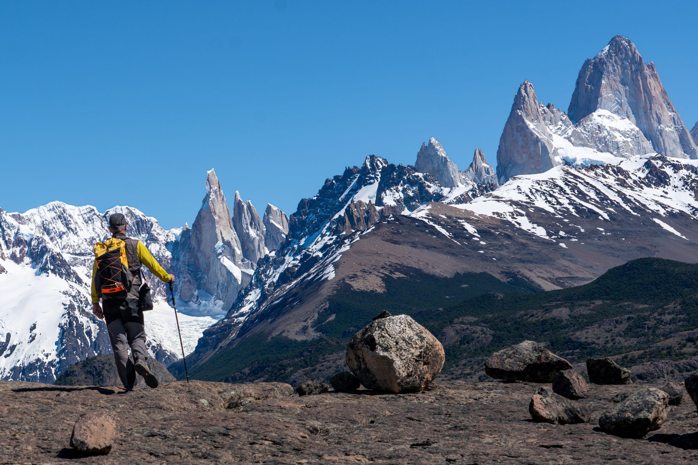 I'm waking towards a mountain range across a flat slab with sine rounded rocks. The background filled with snow covered jagged peaks. Cerro Torre and Fitzroy prominent