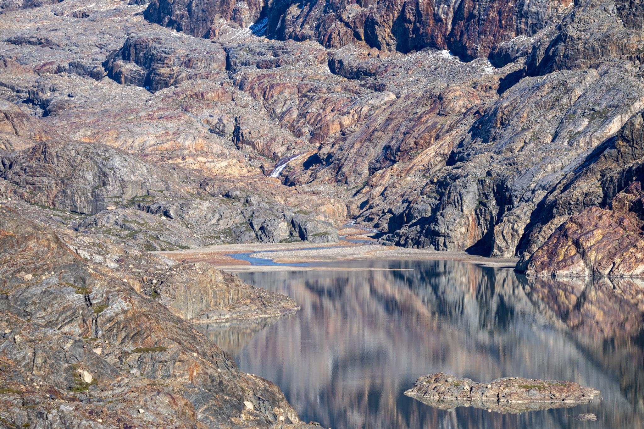 The red and brown colors of the rocks reflected back in Lago Electrico. At the far end of the lake a flat around of ground signifies the position of La Playita, a popular camp for those en route to the Patagonian Icecap