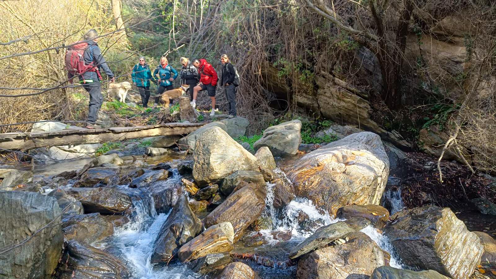 Hikers cross a bridge across a river with boulders