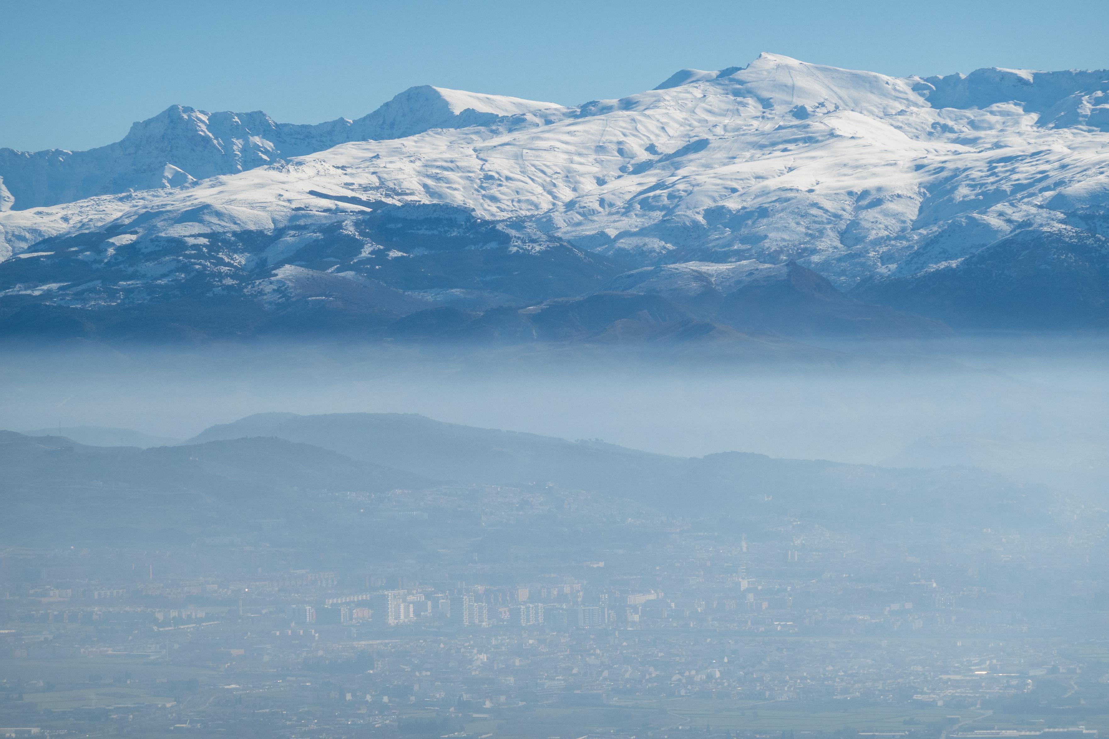 Lower half has outlines of  a city in haze, the upper have snow covered mountains