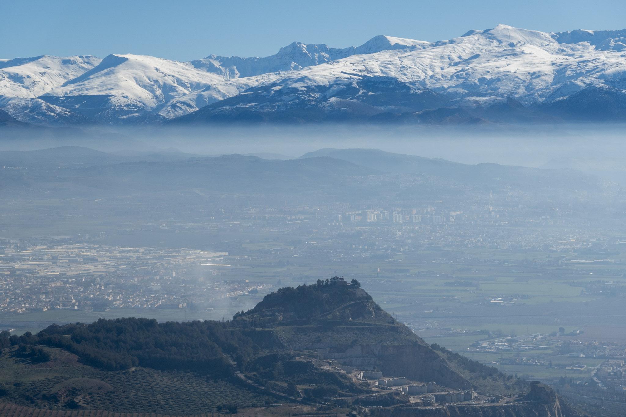 Granada city is in the low lying mists. The Sierra Nevada mountains rise above and are snow covered.